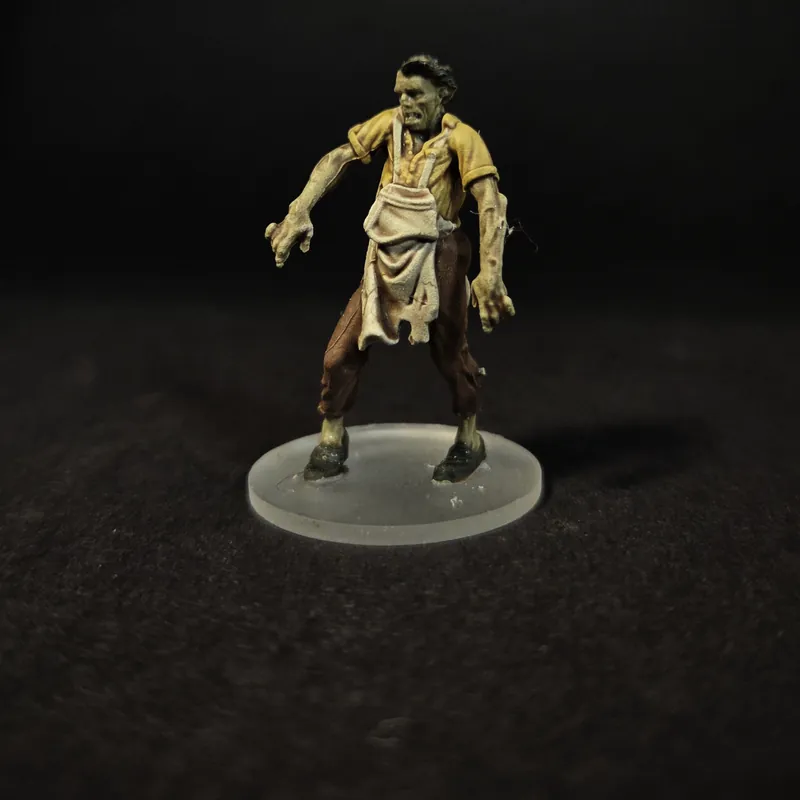 Un zombie en chemise jaune et tablier beige, les bras tendus, sur un socle transparent.